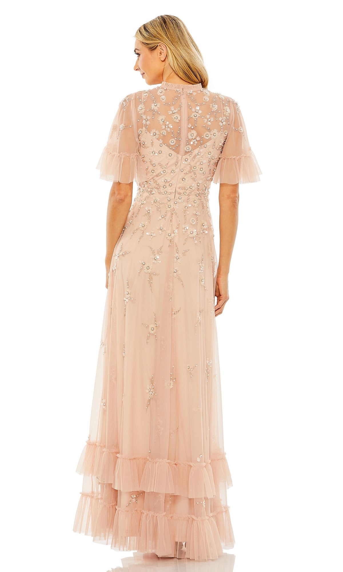 Woman shown from the back wearing the Mac Duggal 9199 Short Sleeve Beaded Formal Gown—a floor-length, light pink sheer evening dress with floral embroidery, short ruffled sleeves, and tiered hem ruffles.